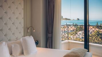 Una habitación de hotel con cama, vista al mar y balcón con barandilla.