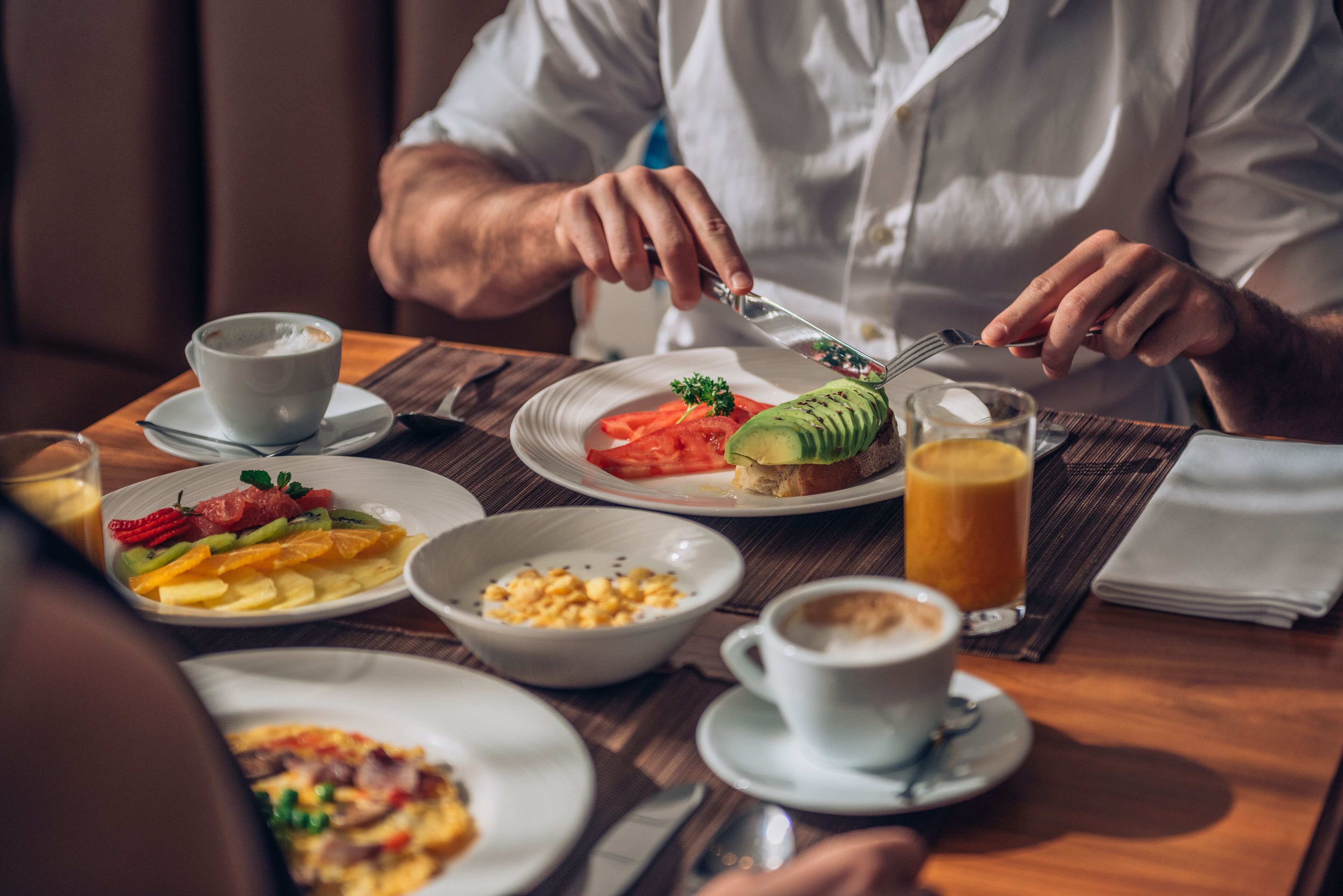 Desayuno con diversas opciones, incluyendo tostadas con aguacate, fruta y huevos revueltos, además de café y jugo.