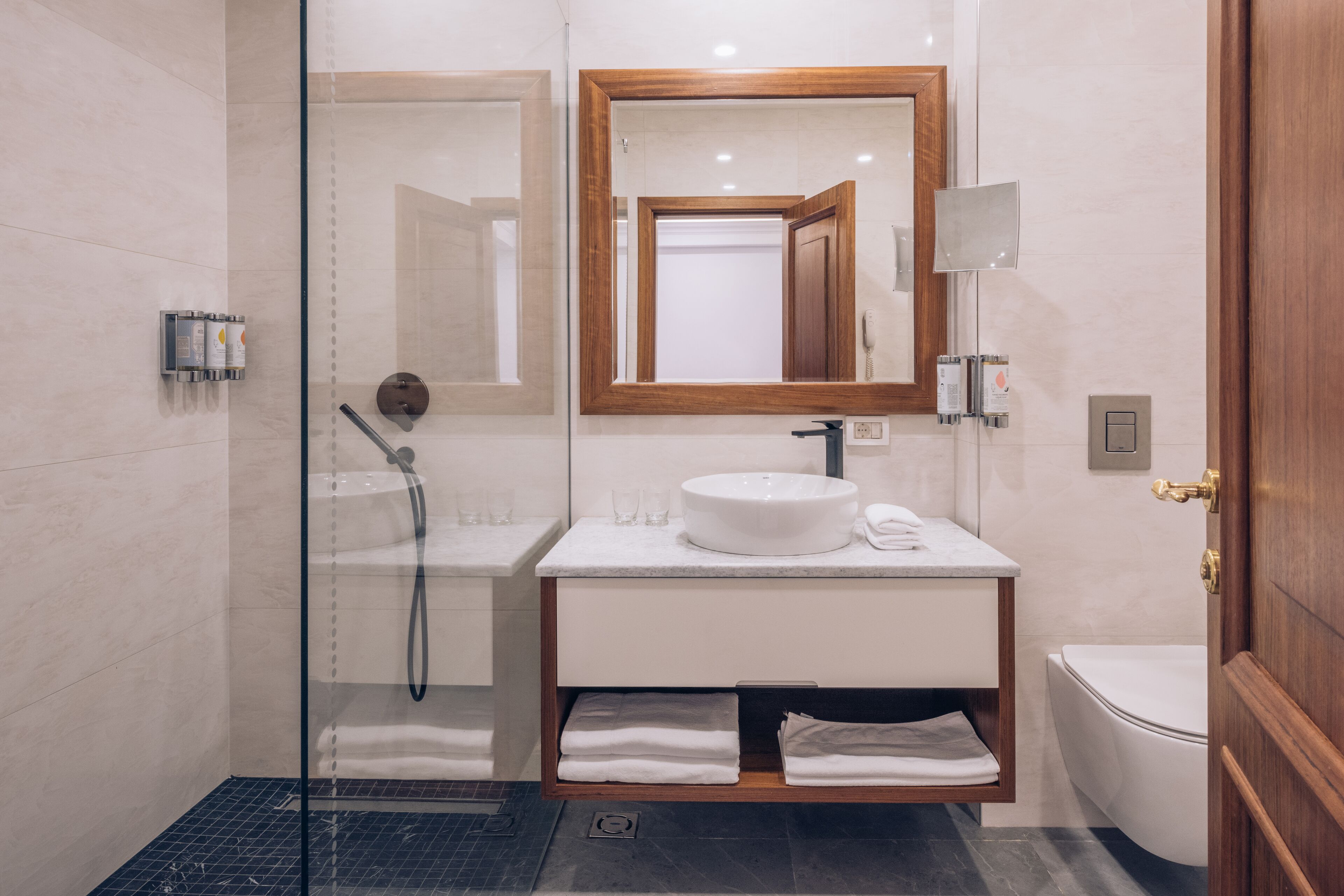 A modern bathroom with a glass-enclosed shower, a white sink with a wooden vanity, and a toilet.