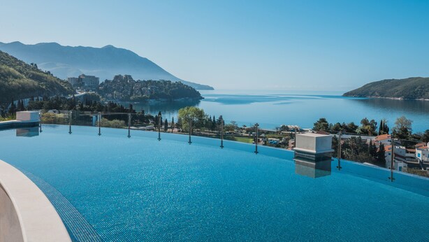Une piscine à l’eau d’un bleu cristallin, entourée de bâtiments et bordée d’un paysage montagneux.