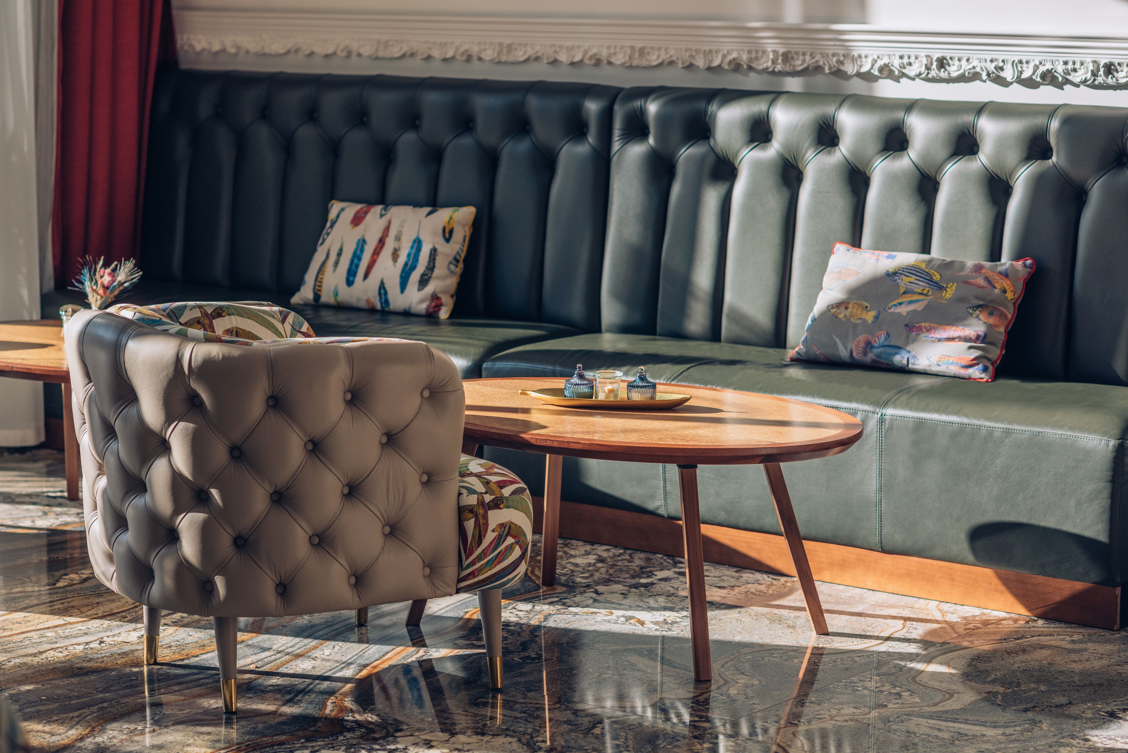 A luxurious seating area with a tufted armchair, a round wooden table, and a green sofa with patterned cushions.