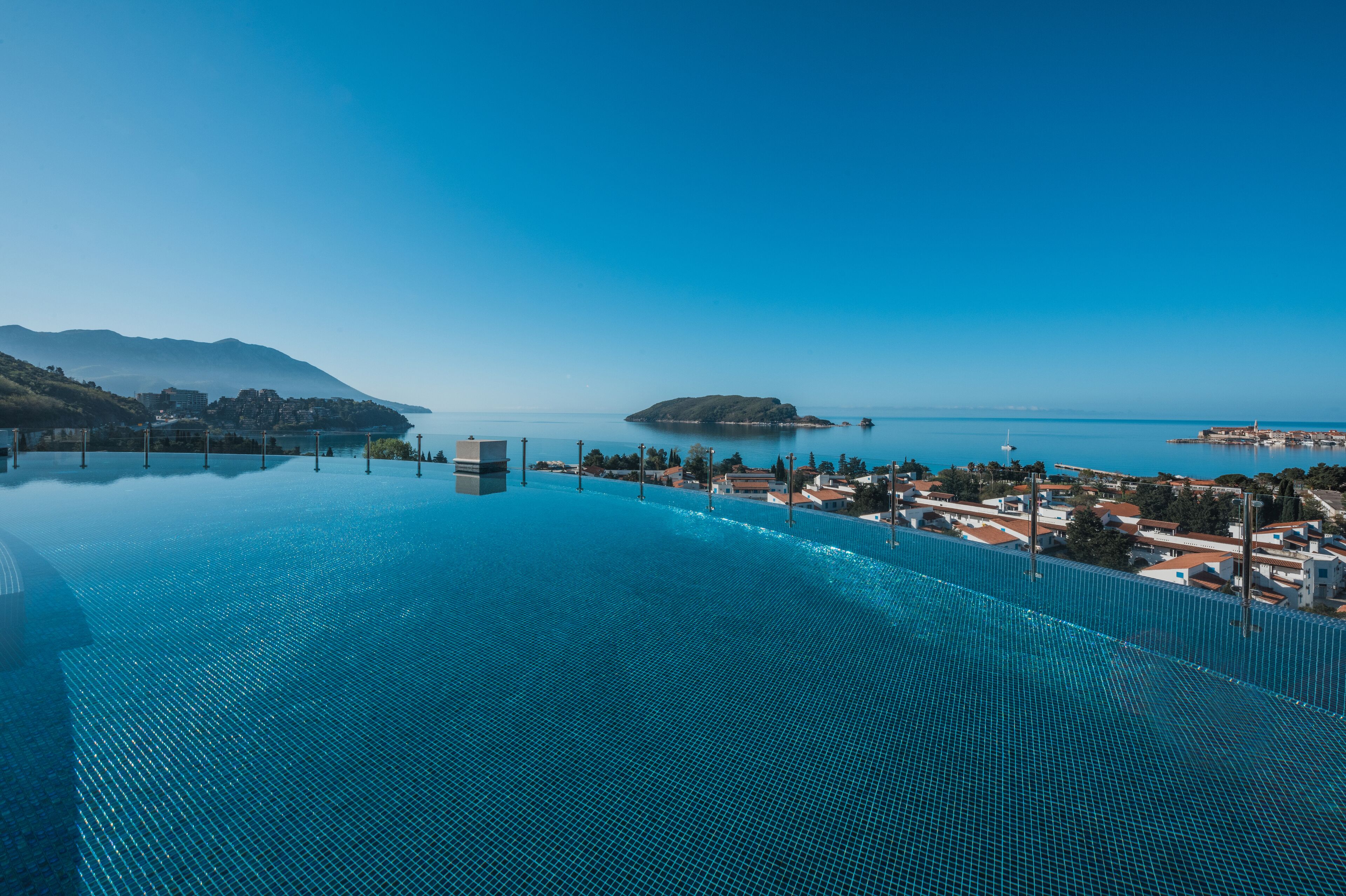 A large infinity pool with a clear view of a coastal town and a distant island.