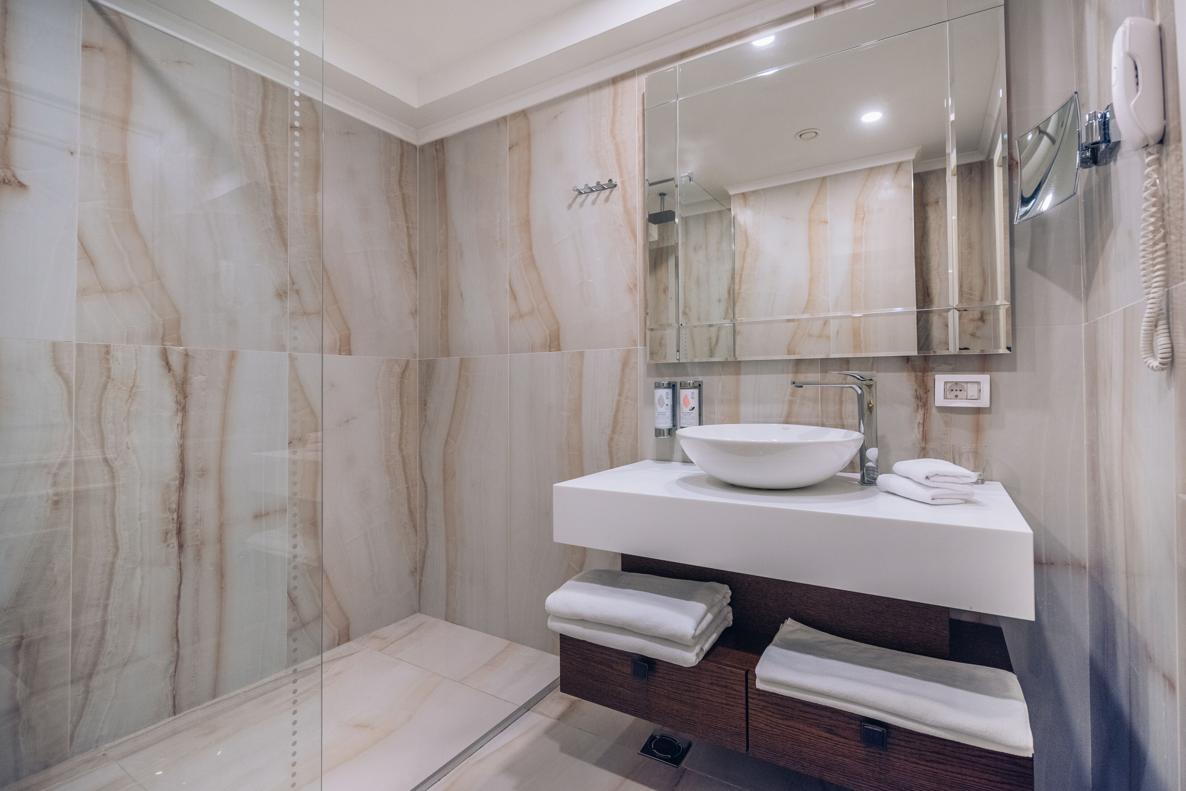 Un baño moderno con un espejo grande, un lavamanos blanco y una cabina de ducha con paredes de vidrio.