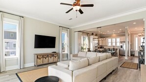 A spacious living room with a large sofa, a flat-screen TV, and a ceiling fan. - Family Friendly Escape -Waterfront, Firepit, 3 Masters, Fishing, Kayaks & More (Navarre)