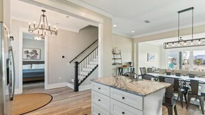 A spacious kitchen with a central island, a dining area with a large table, and a staircase leading to a bedroom. - Family Friendly Escape -Waterfront, Firepit, 3 Masters, Fishing, Kayaks & More (Navarre)