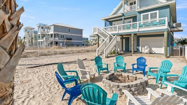 A beachfront property with a two-story house, a fire pit, and several Adirondack chairs. - Family Friendly Escape -Waterfront, Firepit, 3 Masters, Fishing, Kayaks & More (Navarre)