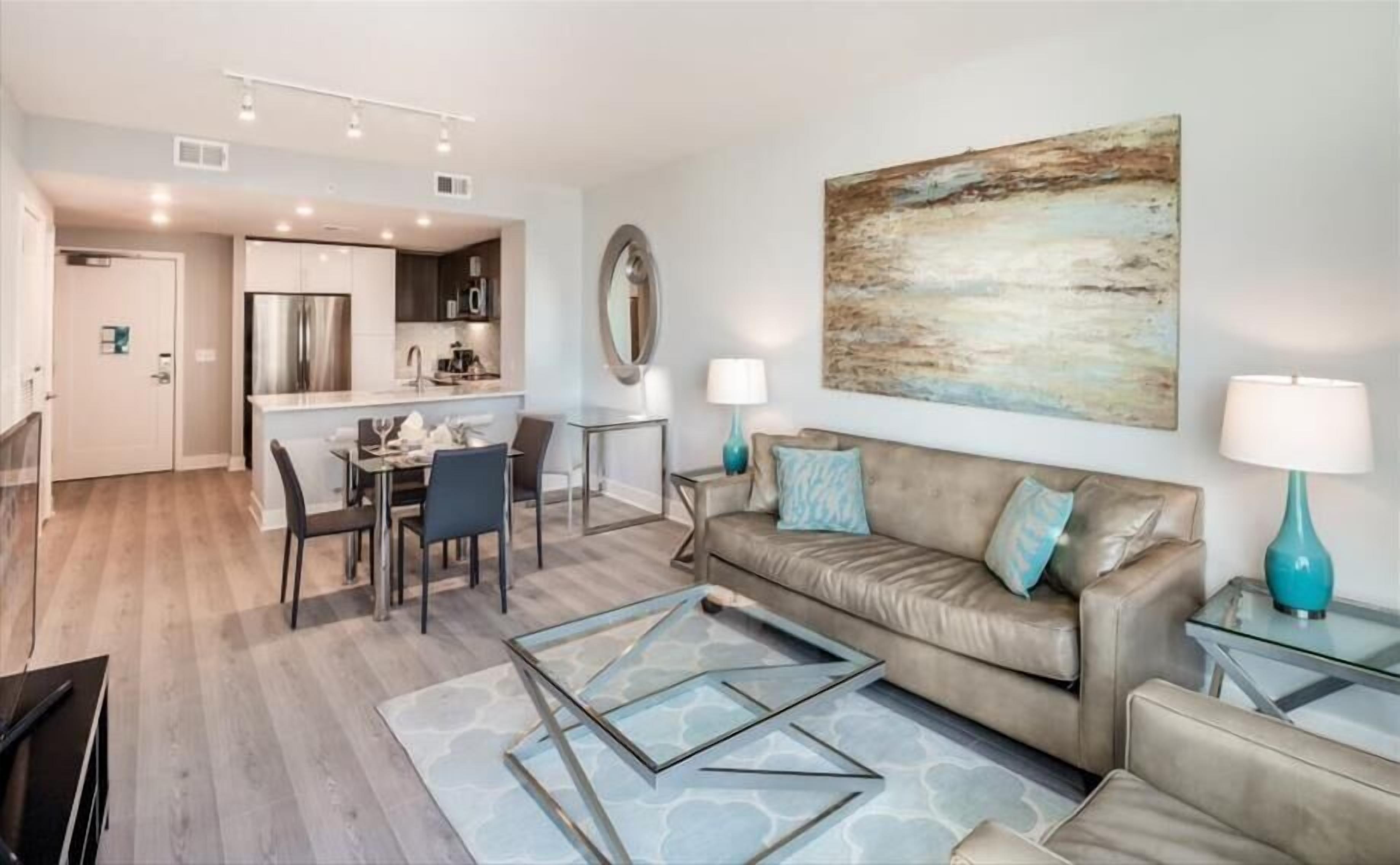 A modern living room with a leather sofa, glass coffee table, and a dining area with a glass table and chairs.