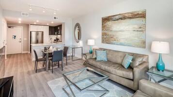 A modern living room with a leather sofa, glass coffee table, and a dining area with a glass table and chairs.