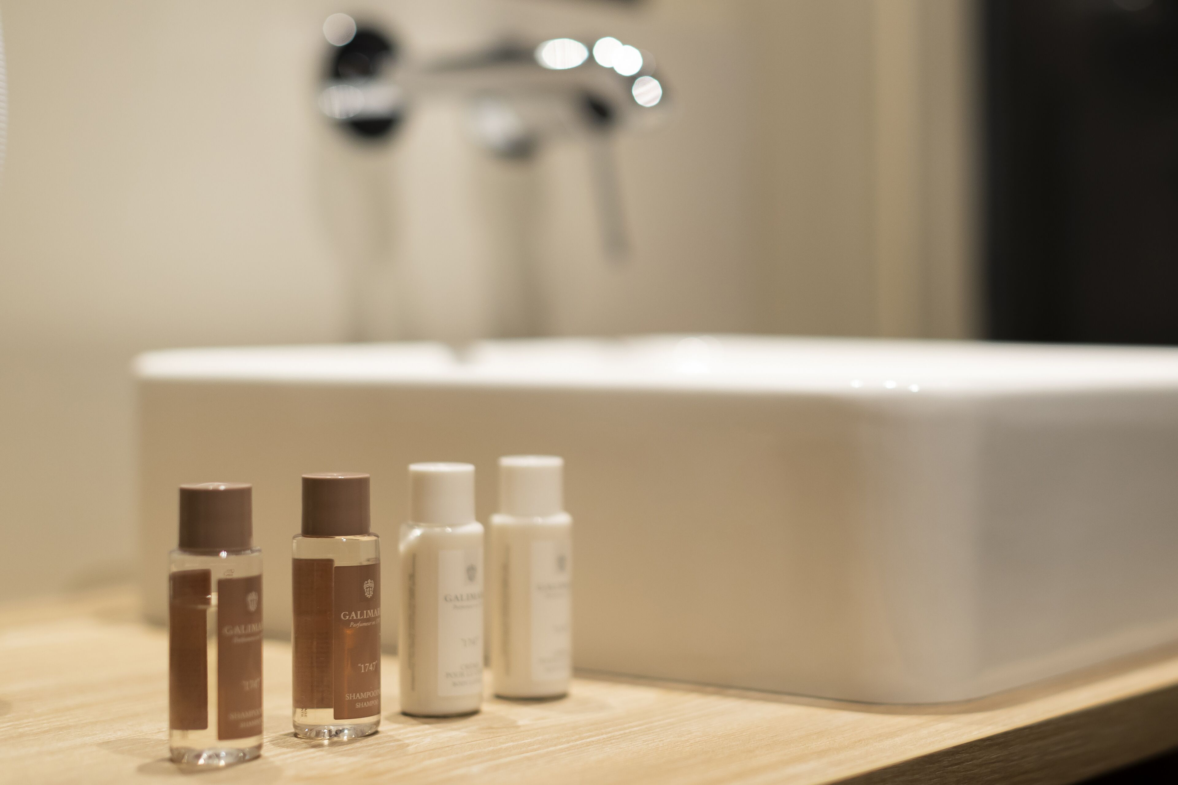 A bathroom with a white sink and four bottles of shampoo on the countertop.