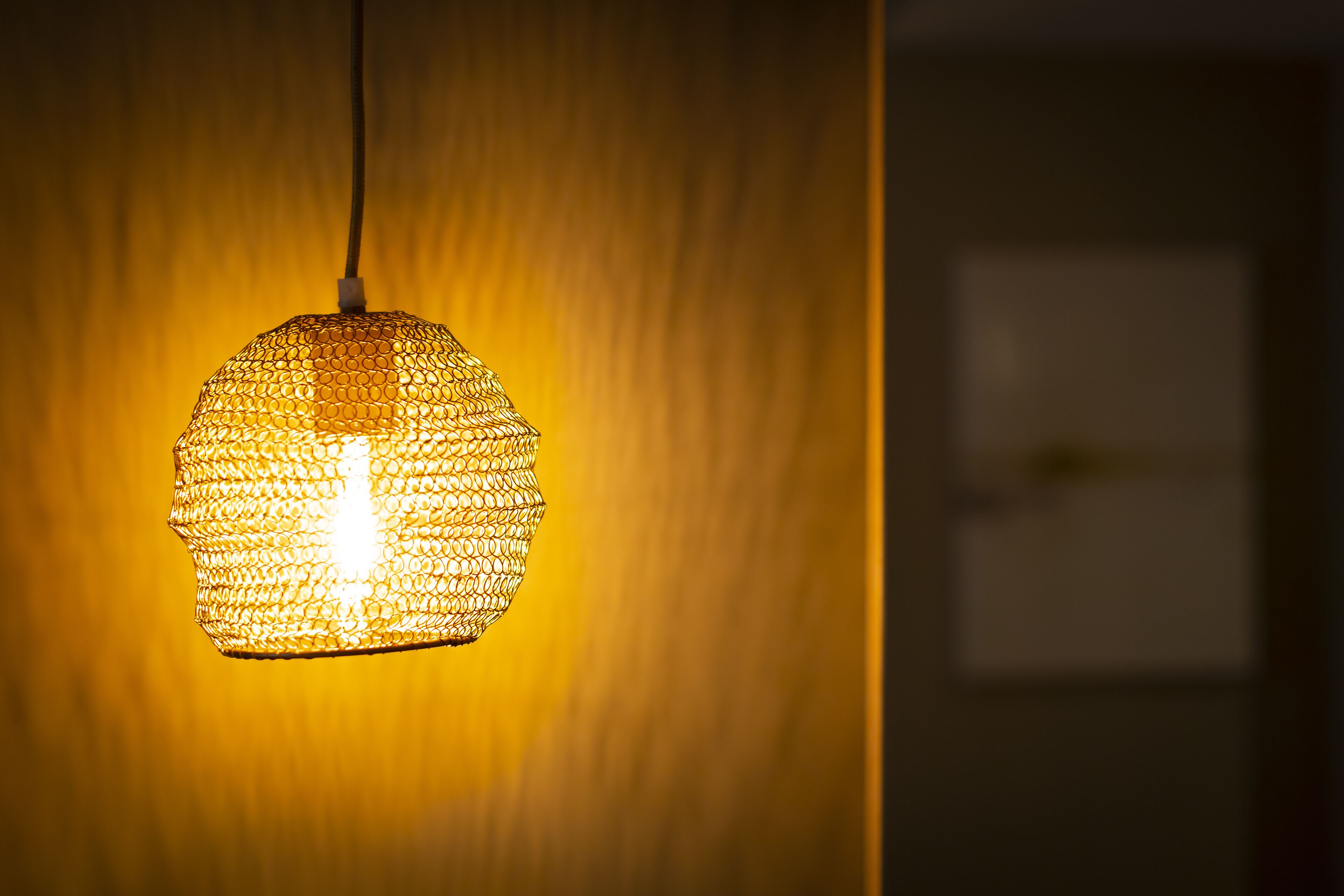 A hanging light fixture with a honeycomb design against a textured wall.