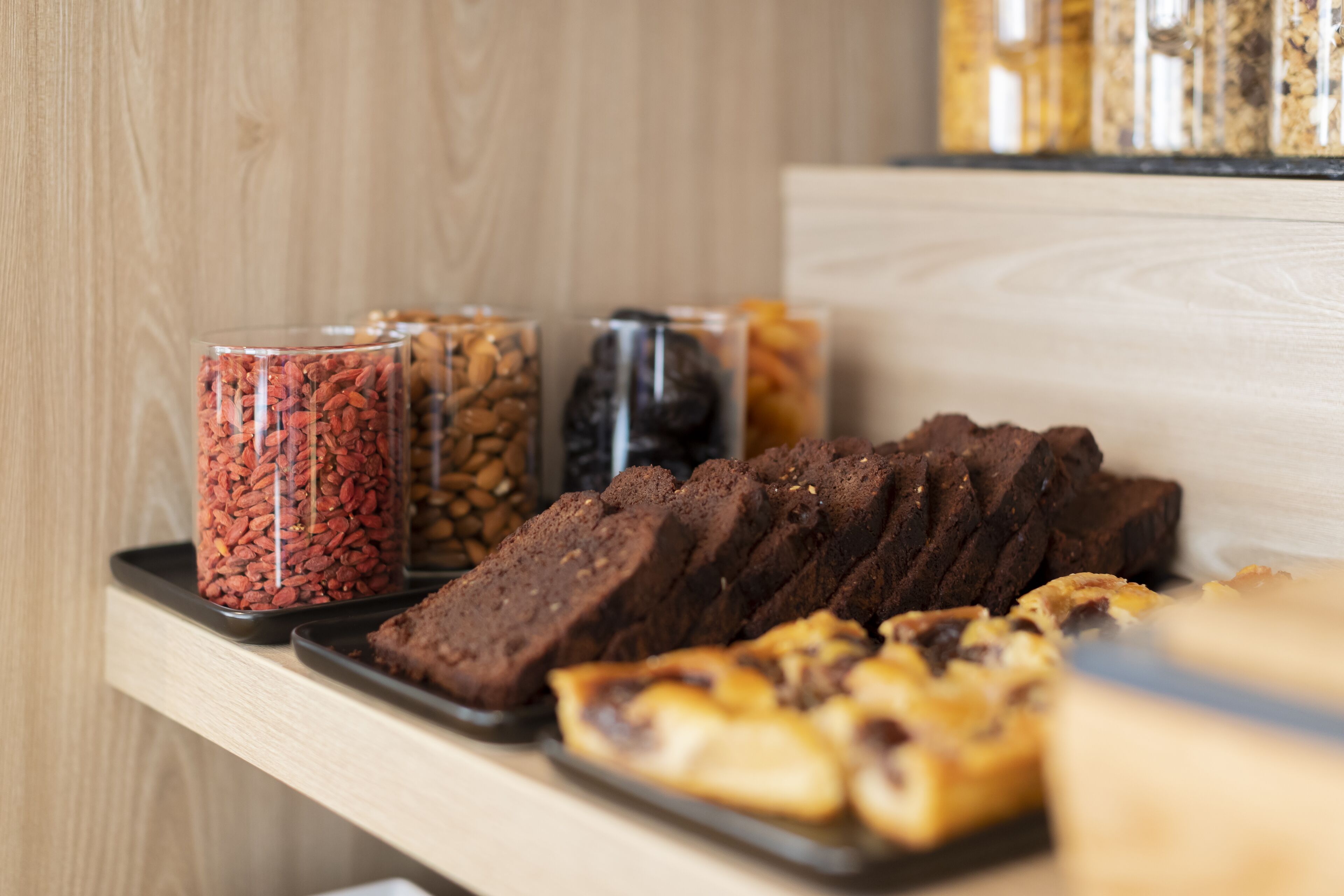 A tray of baked goods and jars of nuts on a wooden surface.