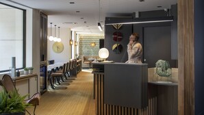 A modern reception area with a wooden reception desk, seating area with chairs and tables, and decorative wall elements. - 37 Lodge La Défense Courbevoie (Courbevoie)