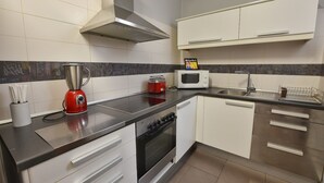 Une cuisine moderne équipée d’une cuisinière à gaz, d’un four à micro-ondes et d’un grille-pain rouge. Les meubles de rangement sont blancs et la hotte est en acier inoxydable.