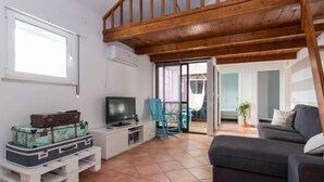 A living room with a television, a sofa, and a wooden ceiling. There are suitcases on a table and a chair in the corner. - Apartment in Vilamoura (Vilamoura)