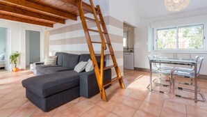 A modern living room with a wooden staircase, a grey sofa, a glass dining table, and a kitchen in the background. - Apartment in Vilamoura (Vilamoura)
