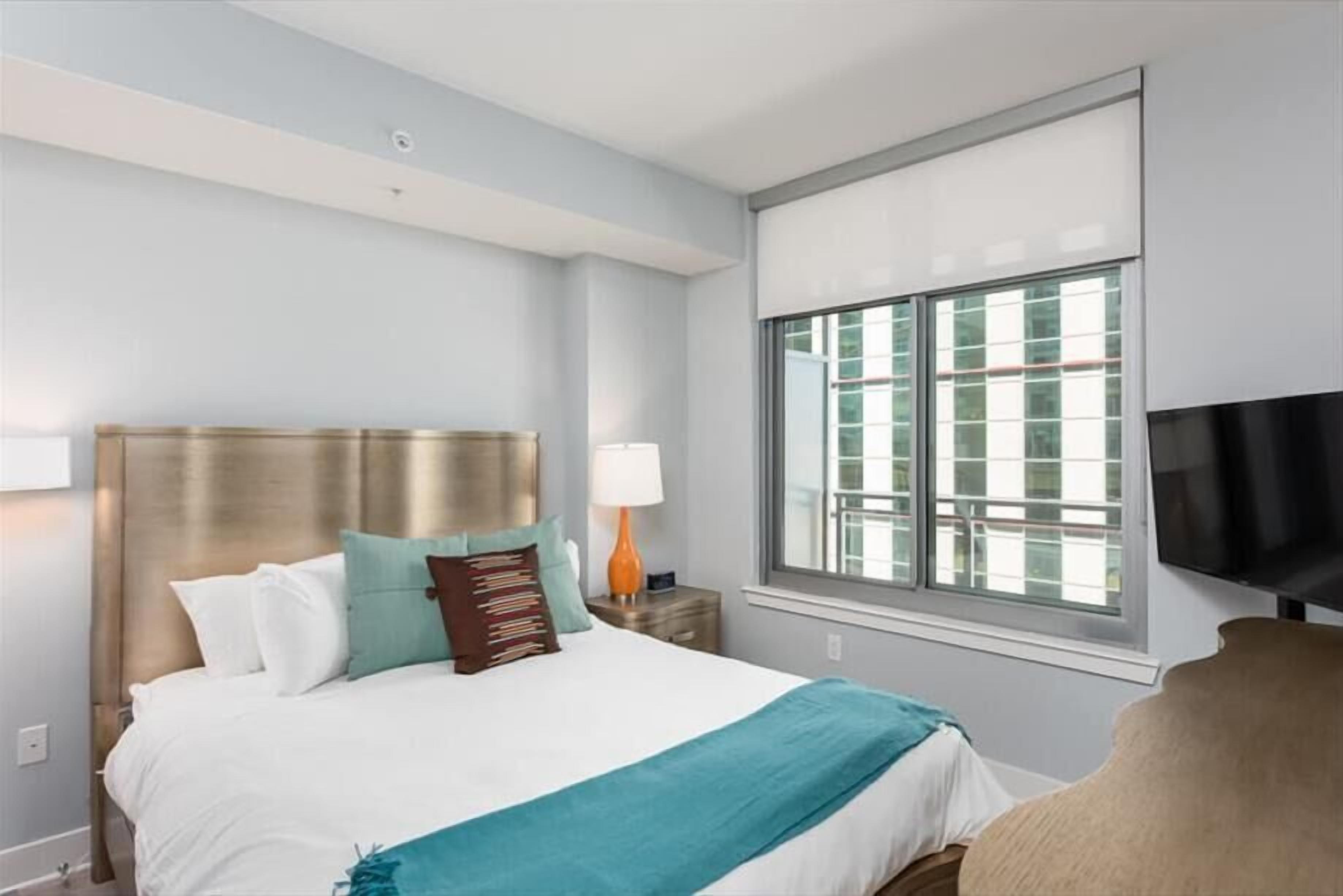 A hotel room with a bed, a TV, a window, and a nightstand.