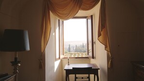 A room with a table and chair, a lamp, and a window with curtains.
