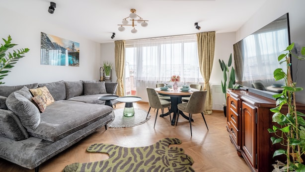 A modern living room with a grey sectional sofa, a dining table with chairs, a zebra-patterned rug, and a large window with curtains. - Apartamenty Sun & Snow Gdynia Centrum (Gdynia)