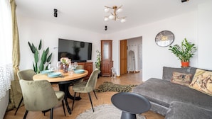 A modern living room with a dining area, a flat-screen TV, and a sofa with decorative pillows. - Apartamenty Sun & Snow Gdynia Centrum (Gdynia)
