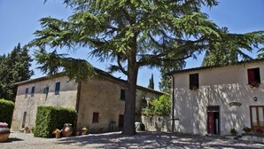 Un edificio rustico con un cortile in ghiaia, circondato da alberi maturi e piante in vaso.