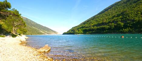 A clear view of a pebble beach leading to calm waters, surrounded by lush green hills.