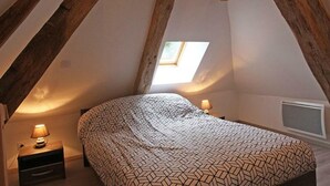 Une chambre avec un plafond en pente, un puits de lumière, un lit avec une literie à motifs, une table de chevet avec une lampe et une petite fenêtre.