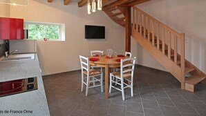Un coin repas agrémenté d’un escalier en bois, d’un téléviseur fixé au mur et d’une fenêtre donnant sur un paysage verdoyant.