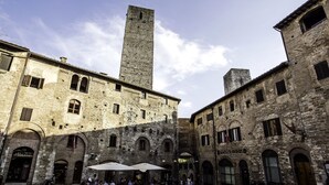 Une place historique bordée de bâtiments en pierre, sur laquelle se dresse une tour imposante, et où l’on trouve des terrasses pour les cafés.