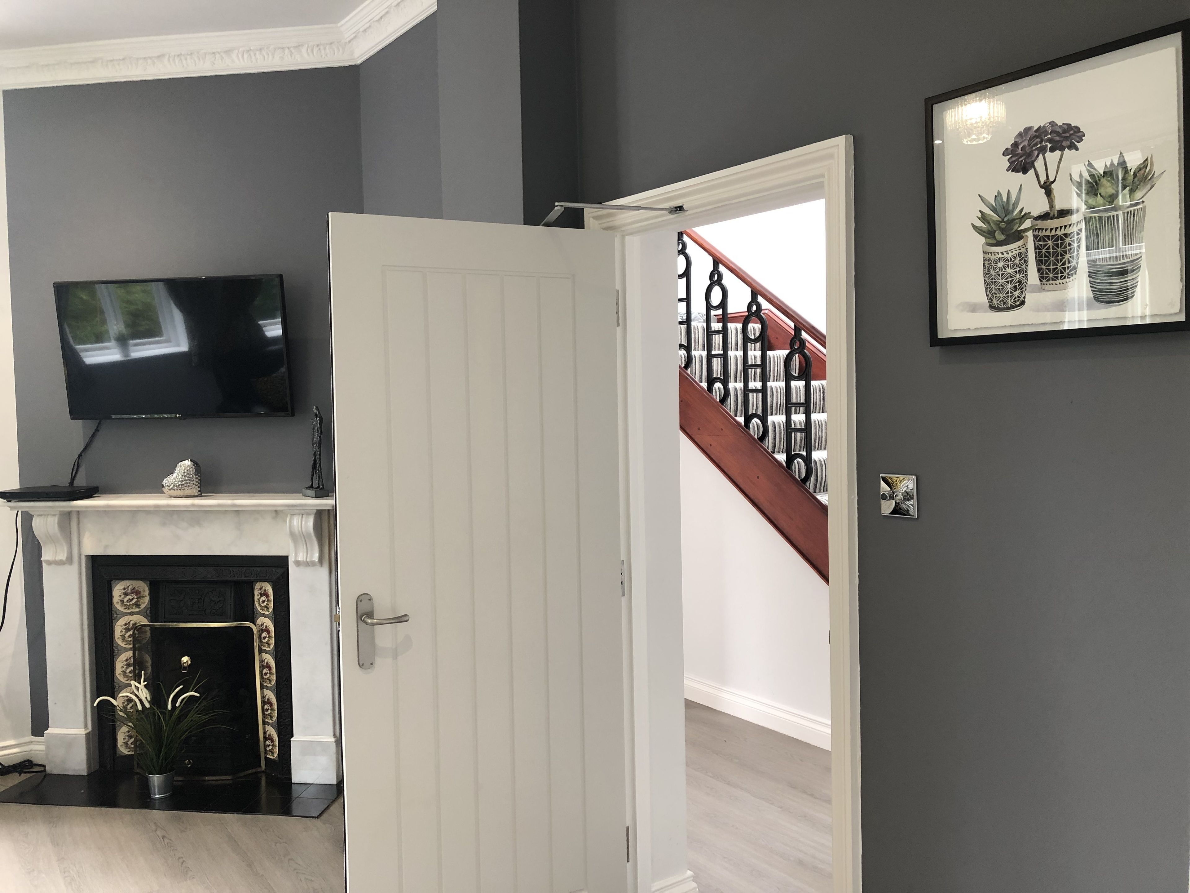 Une pièce avec une cheminée, un téléviseur fixé au-dessus, et une porte donnant sur un escalier.