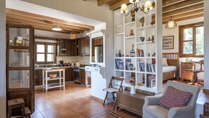A spacious living area with a kitchen, a bookshelf, and a dining area. - Villa Lagoudi Stone House (Λαγουδι Ζία)