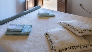 A bedroom with a bed, two pillows, a bedside table, and an open door leading to an outdoor patio with a table and chairs. - Villa Lagoudi Stone House (Λαγουδι Ζία)