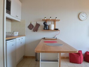 Een kleine keuken met witte kastjes, een houten aanrecht, een koffiezetapparaat en een klok aan de muur.