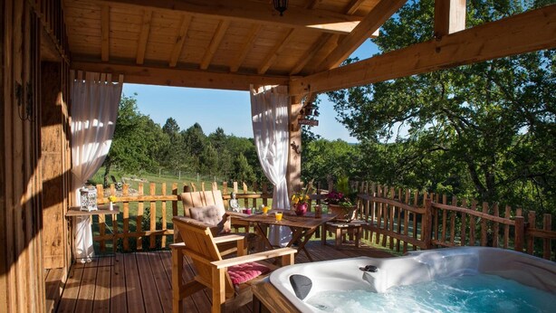 Una terraza de madera con un jacuzzi, sillas y una mesa con decoración exterior.