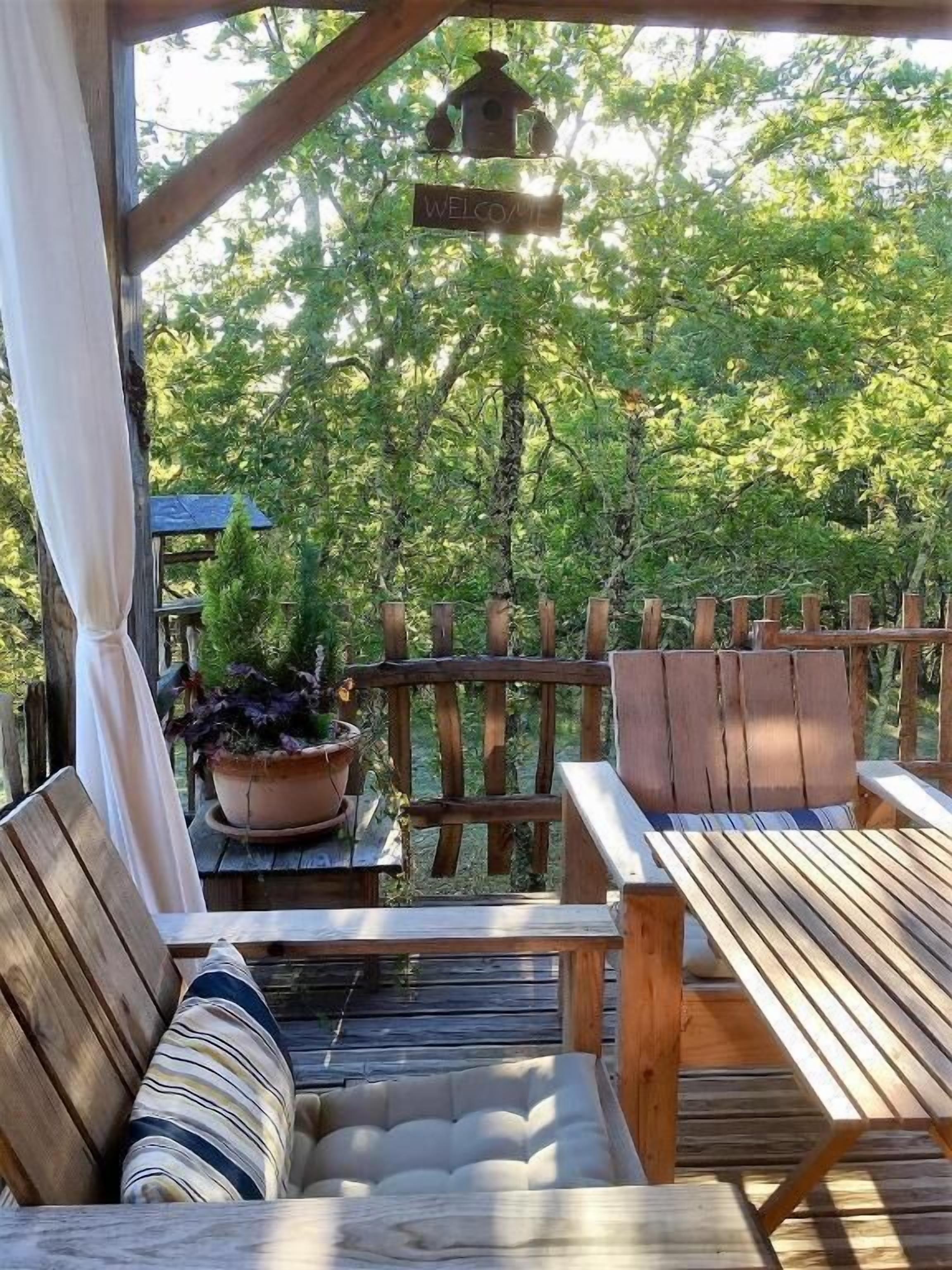A wooden deck with a bench and table, surrounded by a wooden fence, and a 'Welcome' sign hanging above.