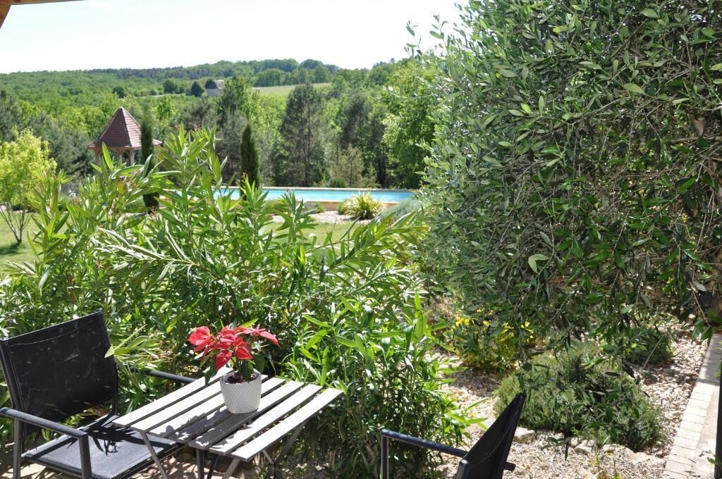 Un patio con mesa y sillas, con vista a una piscina y abundante vegetación.