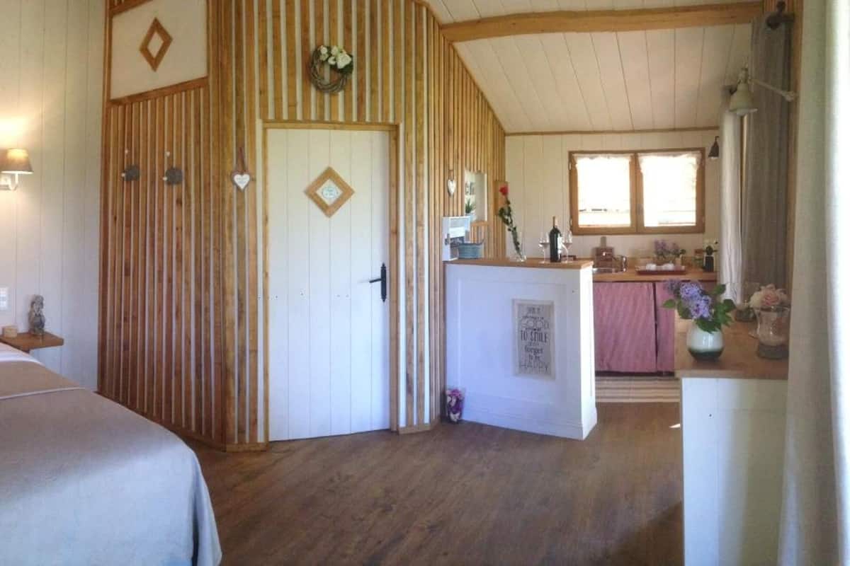 A cozy bedroom with a bed, bedside lamps, a wooden door, and a view into the kitchen area.