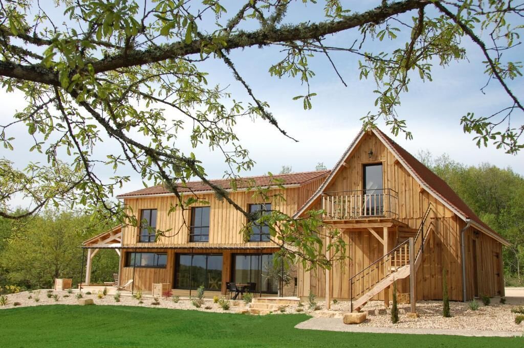 A wooden cabin with a balcony, large windows, and a covered patio area.