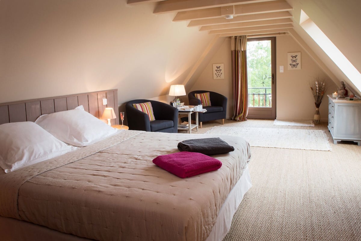 A bedroom with a large bed, a desk, a chair, and a view of the outdoors.