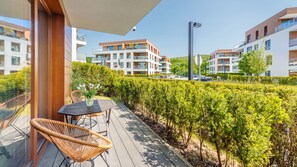 Un balcon avec une table et des chaises, une haie et, au fond, des immeubles d’appartements modernes.