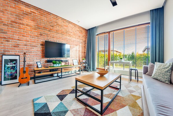 Un salon moderne avec un mur en briques, un téléviseur à écran plat, une table basse en bois, un canapé et un tapis coloré.