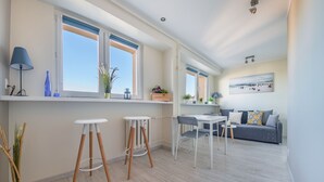 Una sala moderna con un sofá gris, una mesa de comedor blanca y dos taburetes de madera.