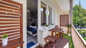 Un balcón con una mesa y sillas de madera, una pequeña planta en maceta y vistas a un edificio con aguja.