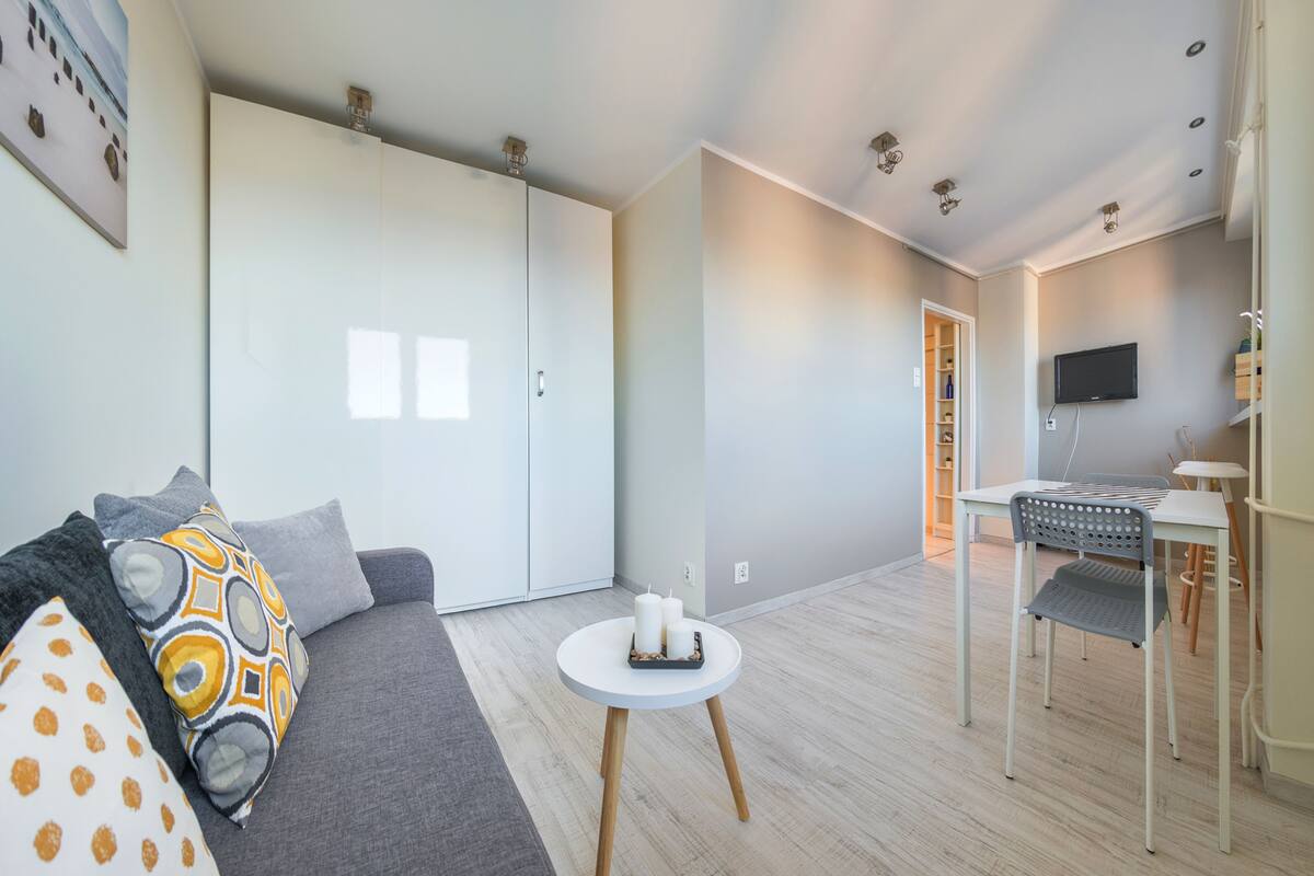 A modern living room with a grey sofa, a small round table with candles, and a TV mounted on the wall.