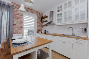 A modern kitchen with white cabinets, a brick accent wall, and a wooden dining table set for two. - ShortStayPoland Marymoncka - B22 (Warsaw)
