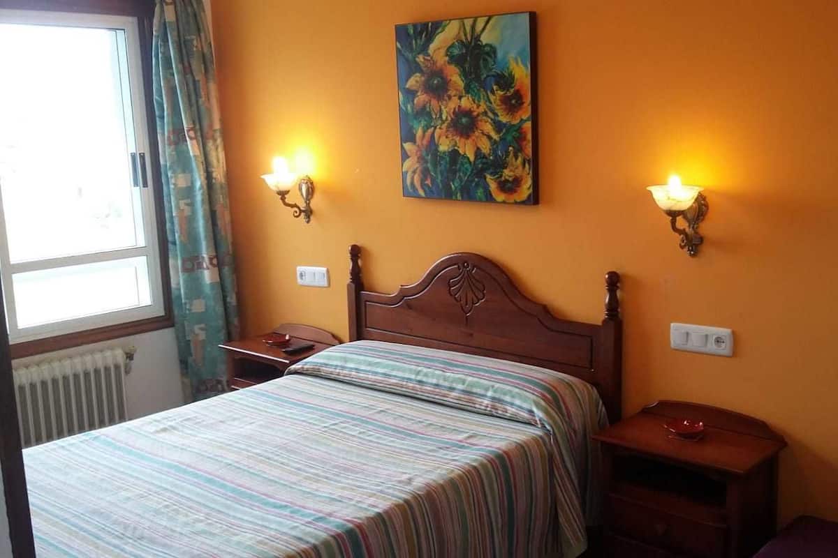 Um quarto com uma cama, duas mesas de cabeceira, um criado-mudo, um quadro na parede e duas luminárias de parede.