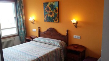 Un dormitorio con una cama, dos mesitas de noche, una lámpara de noche y un cuadro en la pared, además de dos lámparas fijadas a la pared.