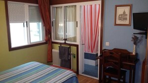 Un dormitorio con cama, una ventana con cortinas, un radiador, una silla de madera y un cuadro en la pared.