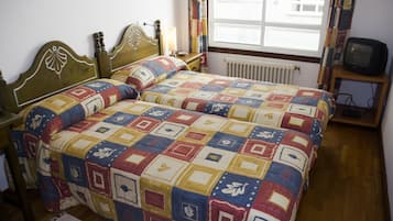 A bedroom with a wooden bed, a bedside table, a chair, a television, and a window with curtains.
