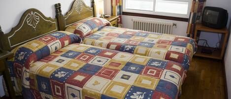Un dormitorio con una cama de madera, una mesita de noche, una silla, un televisor y una ventana con cortinas.