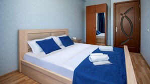 A neatly made bed with blue and white bedding, a wooden headboard, and a blue throw blanket. - Penta Tbilisi (Tbilisi)